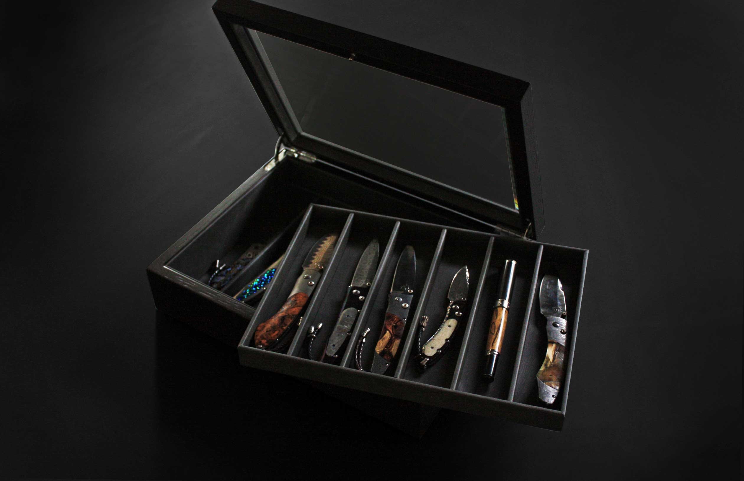Dark Collectors Deluxe Display Case with glass lid, open to show various folding knives and a pen within compartmentalized trays.