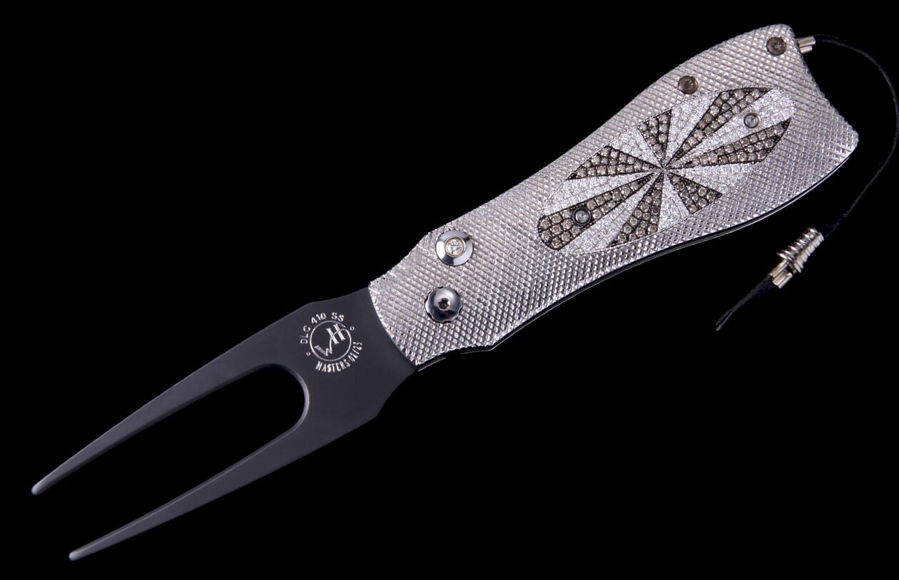 Luxury golf divot tool with silver textured handle, starburst pattern of clear and brown diamonds, and black fork.