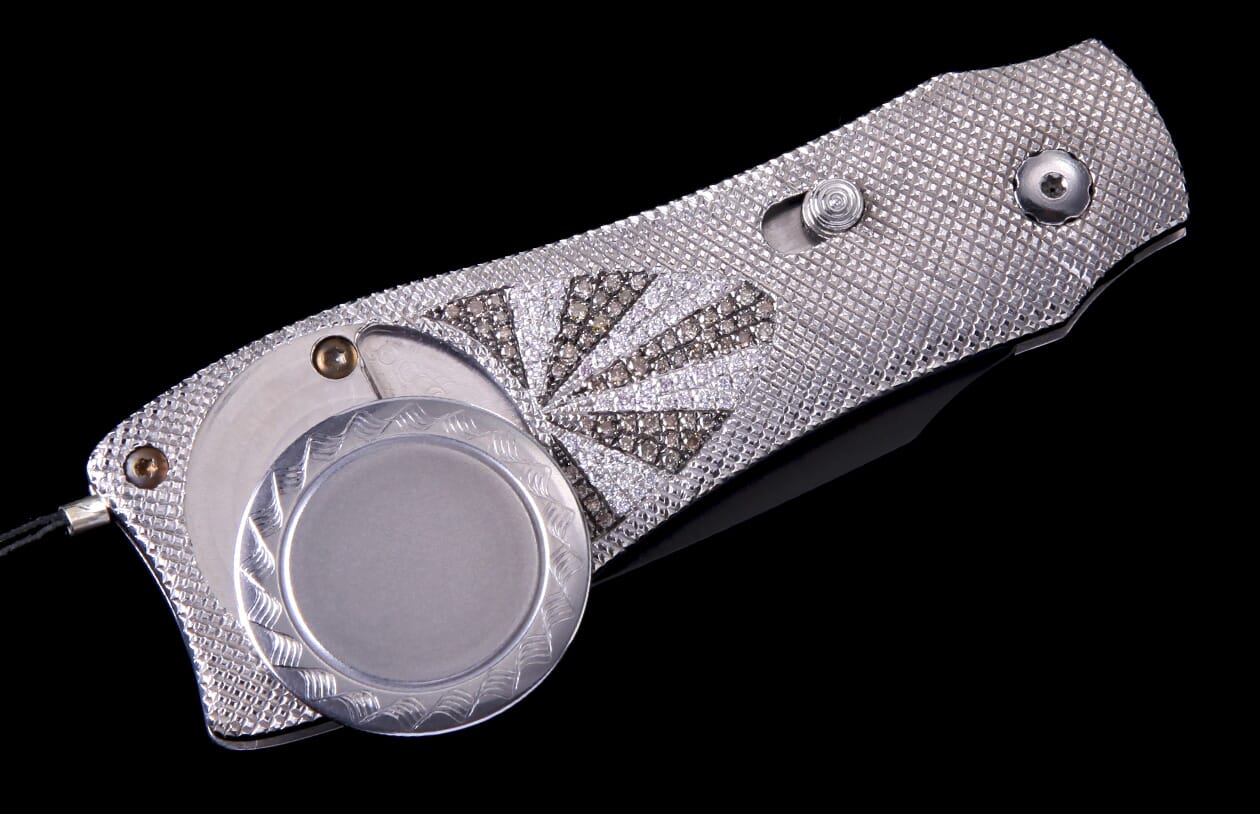 Ornate silver folding knife with a white and brown diamond sunburst pattern, a textured handle, and an engraved circular element.