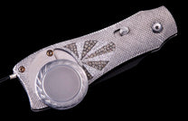 Ornate silver folding knife with a white and brown diamond sunburst pattern, a textured handle, and an engraved circular element.