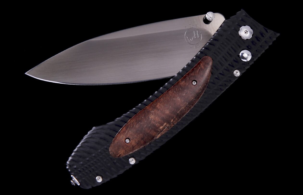 Partially open folding knife with a textured black handle, a brown wood inlay, and a silver blade with a thumb stud.