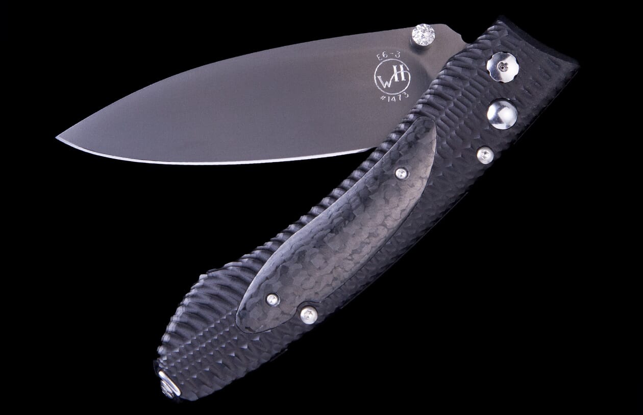 Dark grey folding knife by WH, half-open with a textured handle, polished blade marked "E6-3", and diamond accent.