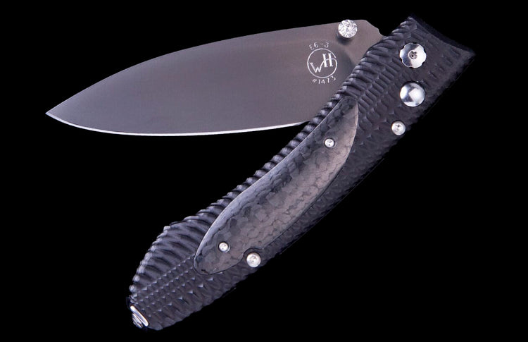Dark grey folding knife by WH, half-open with a textured handle, polished blade marked "E6-3", and diamond accent.