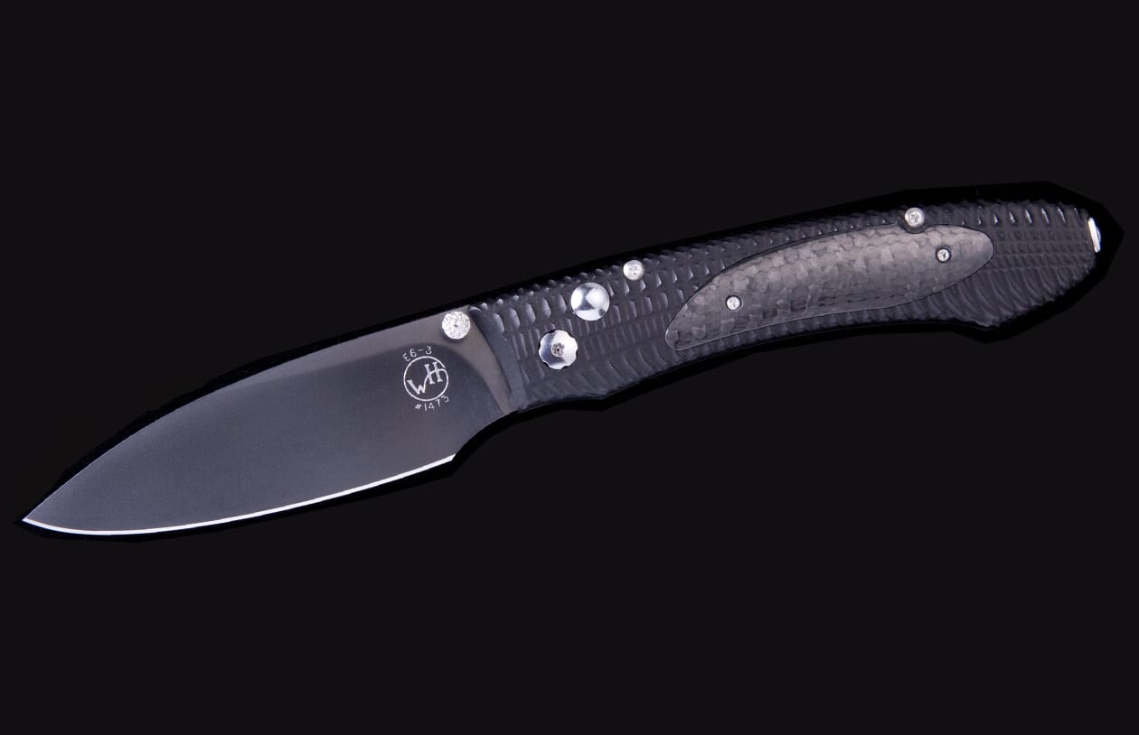 E6 3 folding knife with a dark blade and a dark carbon fiber handle featuring textured patterns and engraved markings.