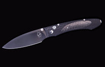 E6 3 folding knife with a dark blade and a dark carbon fiber handle featuring textured patterns and engraved markings.