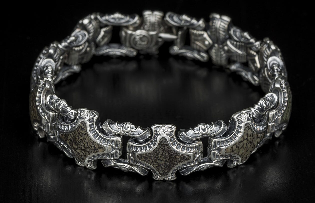 Silver-toned metal bracelet with ornate links, dark textured inlays, and a small clear stone.