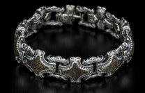 Silver-toned metal bracelet with ornate links, dark textured inlays, and a small clear stone.