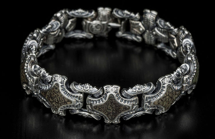 Silver-toned metal bracelet with ornate links, dark textured inlays, and a small clear stone.
