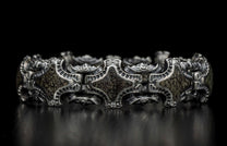 Ornate silver bracelet featuring intricate links, textured dark inserts, and small clear stones, on a reflective black surface.