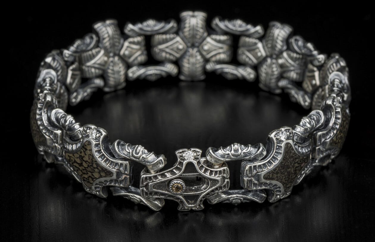 Ornate sterling silver bracelet with intricate links, textured dark brown panels, and a clasp featuring a clear and amber gemstone.