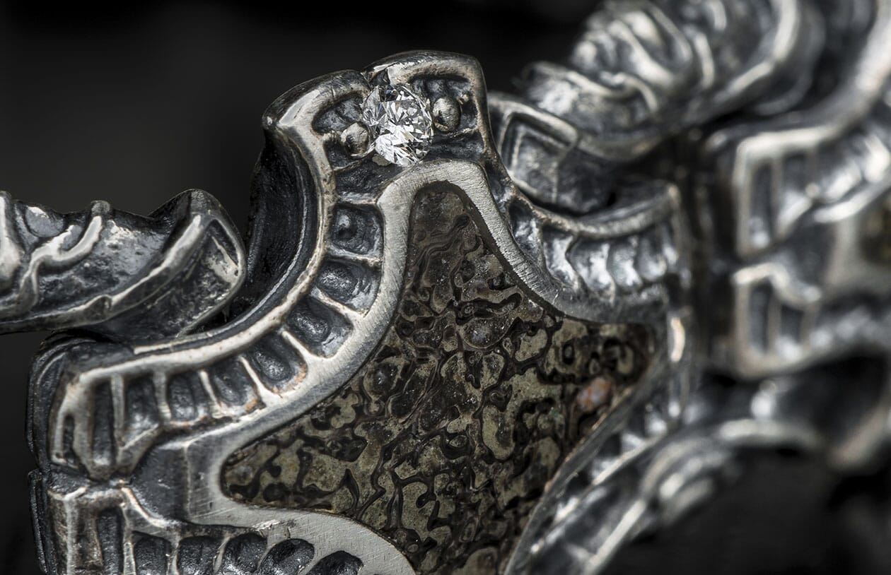 Ornate silver jewelry featuring a sparkling diamond and a dark, organic textured central panel.