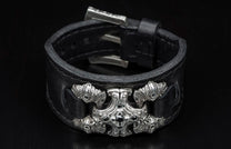 Black leather cuff bracelet with an ornate silver-tone cross-shaped emblem detailed with black stones and a buckle closure.