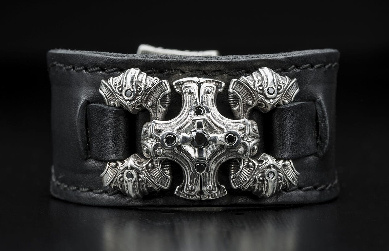Black leather bracelet featuring an ornate silver centerpiece with black gemstones and intricate ram head side accents.