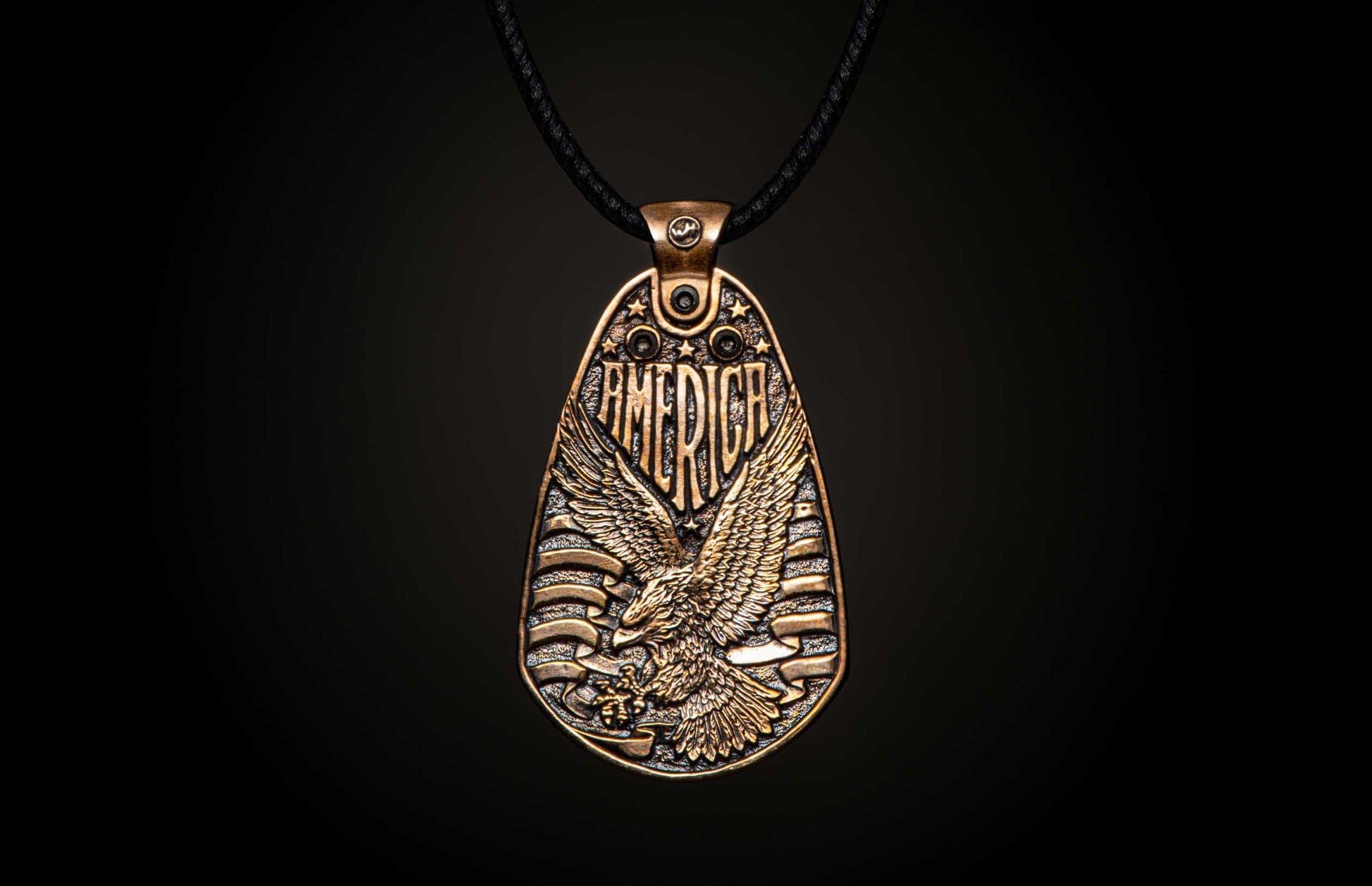 Aged bronze pendant necklace featuring a bald eagle, "AMERICA" text, stars, and stripes, suspended from a black cord.
