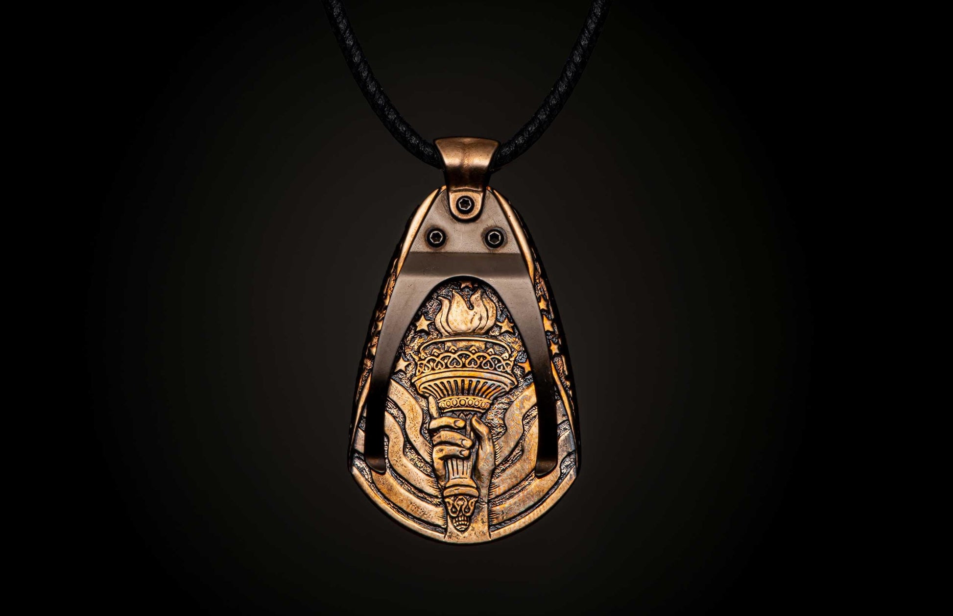 Ornate antique bronzed metal pendant depicting a hand holding a flaming torch surrounded by stars, on a black braided cord.