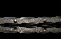 Metallic bracelet with interwoven design and gold accents on a black background