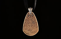 A bronze teardrop pendant by Jekyll + Hyde, featuring intricate leaf and vine carvings with text, hanging from a black cord.