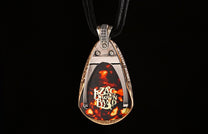 Bronze and silver guitar pick pendant by William Henry with engraved scrollwork, featuring a tortoise-shell pick with 'Zac Brown Band' logo, on a black cord.