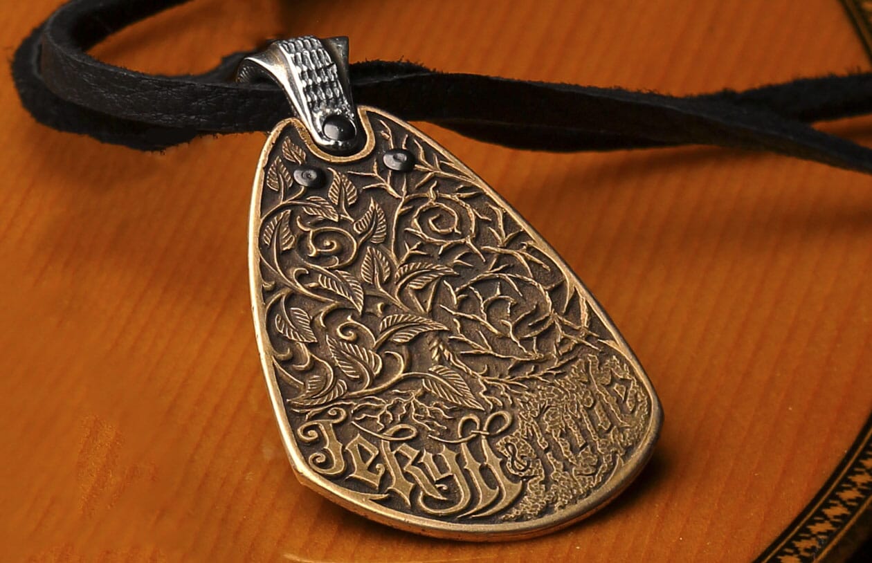 Bronze pendant by Jekyll + Hyde with ornate botanical relief, 'Jekyll' and 'Hyde' text, and black gems on a black strap.