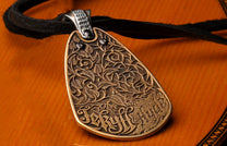 Bronze pendant by Jekyll + Hyde with ornate botanical relief, 'Jekyll' and 'Hyde' text, and black gems on a black strap.