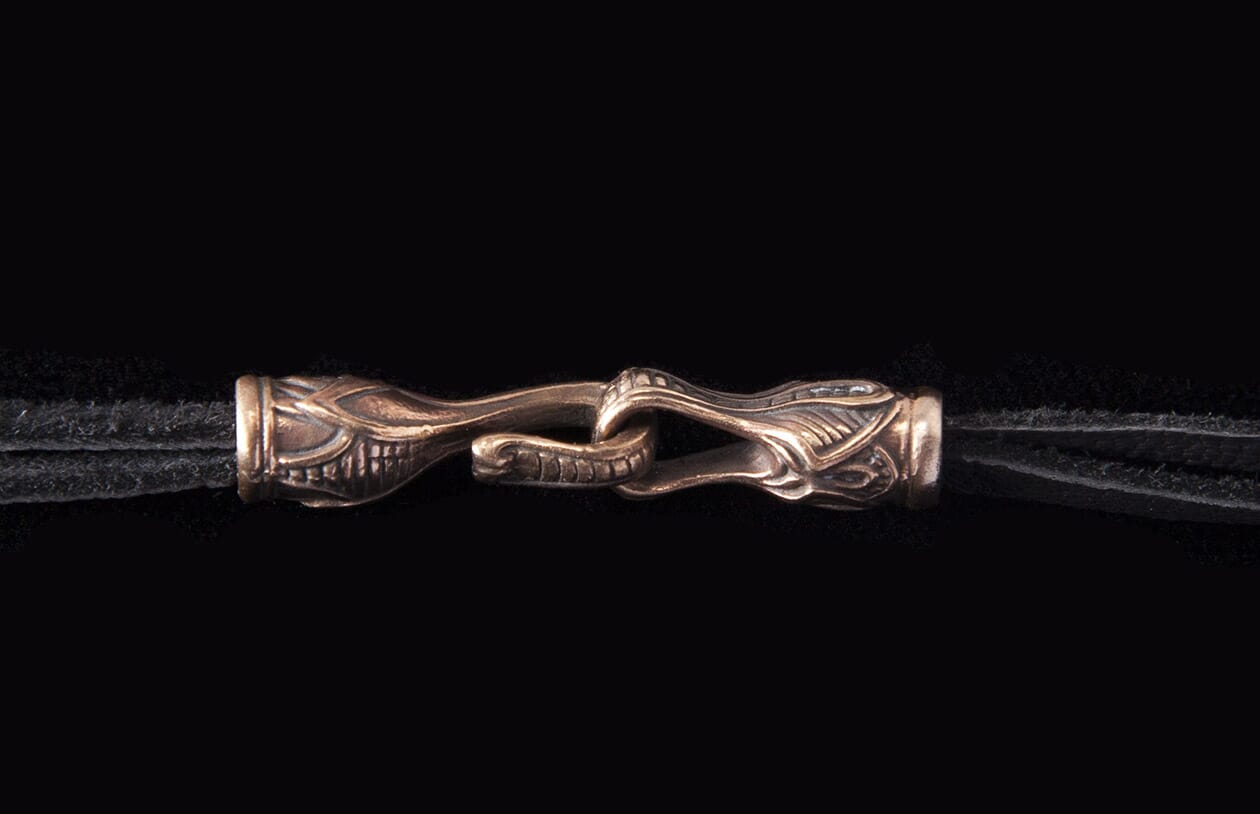 Jekyll + Hyde Bronze Edition jewelry clasp with ornate, stylized interlocking details on a black cord.