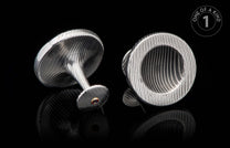 Pair of silver-toned cufflinks with engraved wavy patterns, one featuring a red gemstone in a gold bezel.