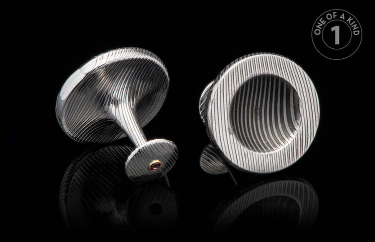 Pair of silver-toned cufflinks with engraved wavy patterns, one featuring a red gemstone in a gold bezel.