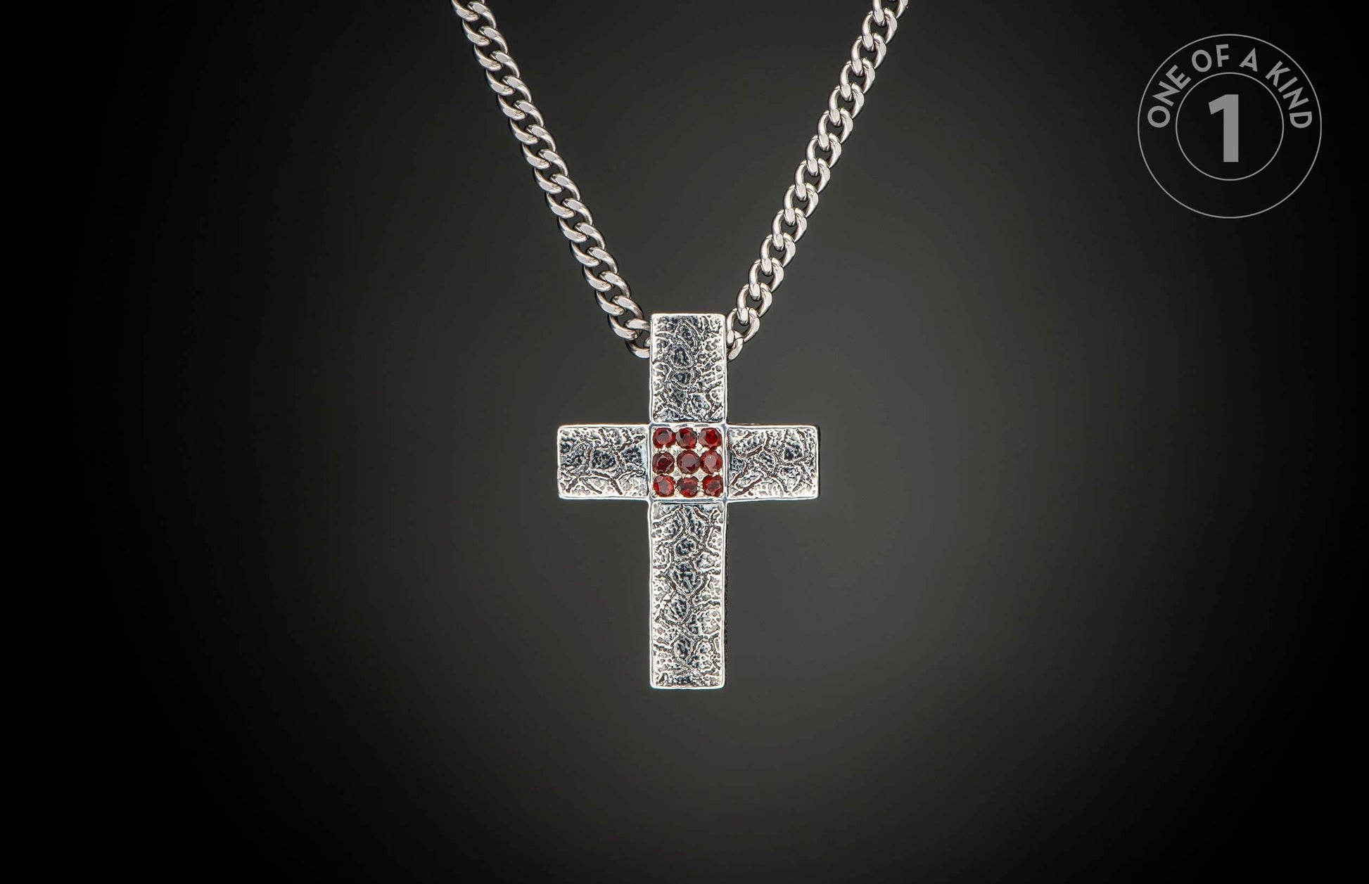 Silver cross pendant with a textured pattern and red gemstones in the center, hanging from a curb chain.