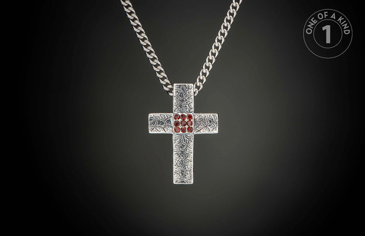 Silver cross pendant with a textured pattern and red gemstones in the center, hanging from a curb chain.