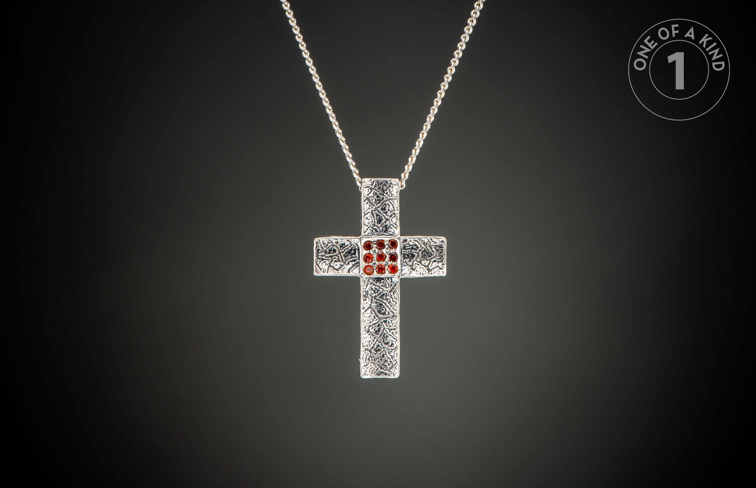 Silver cross pendant necklace with ornate texture, nine central red gemstones, and a "One of a Kind 1" logo.