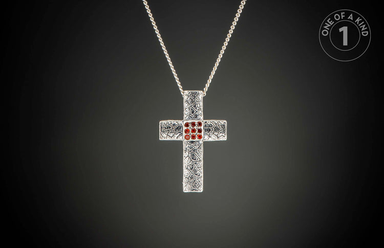 Silver cross pendant necklace with ornate texture, nine central red gemstones, and a "One of a Kind 1" logo.