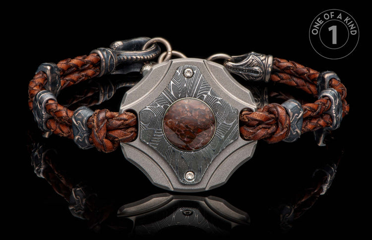 Brown braided leather and dark metal bracelet with a central shield, reddish-brown stone, and intricate Damascus pattern.