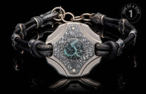 Black leather bracelet with textured metal links and an intricate patterned centerpiece with a blue-green round inlay.