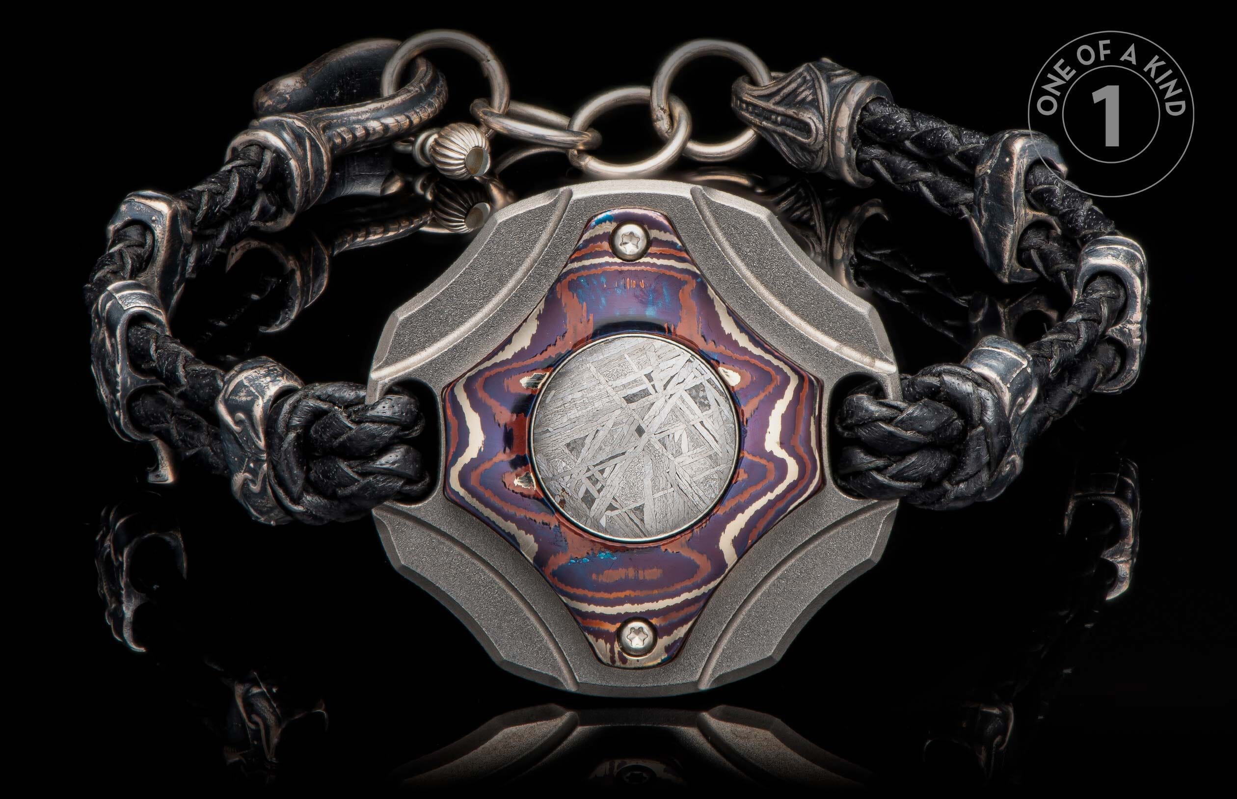 Black braided leather and ornate metal bracelet with a central plaque featuring a colorful inlay and meteorite pattern.