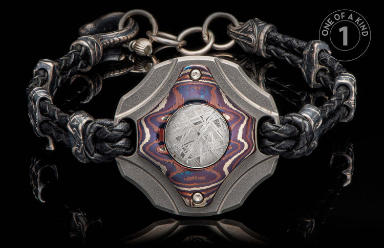 Black braided leather and ornate metal bracelet with a central plaque featuring a colorful inlay and meteorite pattern.