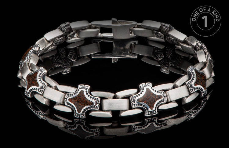 A chunky silver-toned metal bracelet with decorative cross-shaped links featuring brown patterned inlay, on a reflective black surface.