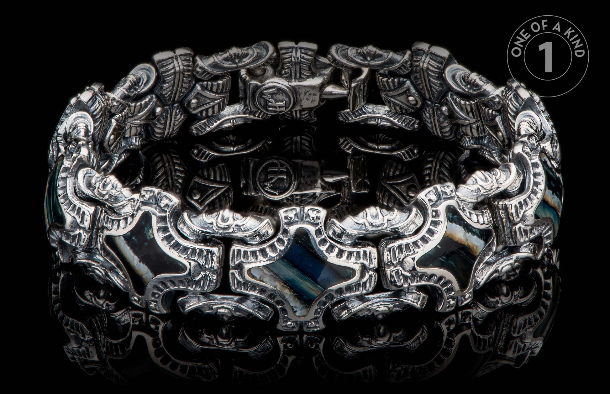 Silver-toned ornate bracelet with intricate embossed patterns, dark iridescent stone inlays, and visible 'HM' initials.