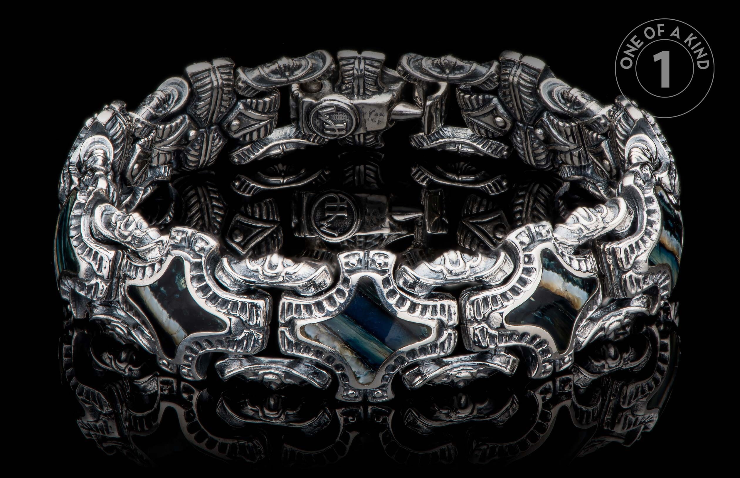 Silver-toned ornate bracelet with intricate embossed patterns, dark iridescent stone inlays, and visible 'HM' initials.