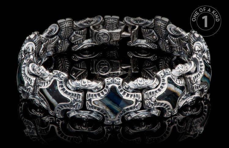 Silver-toned ornate bracelet with intricate embossed patterns, dark iridescent stone inlays, and visible 'HM' initials.