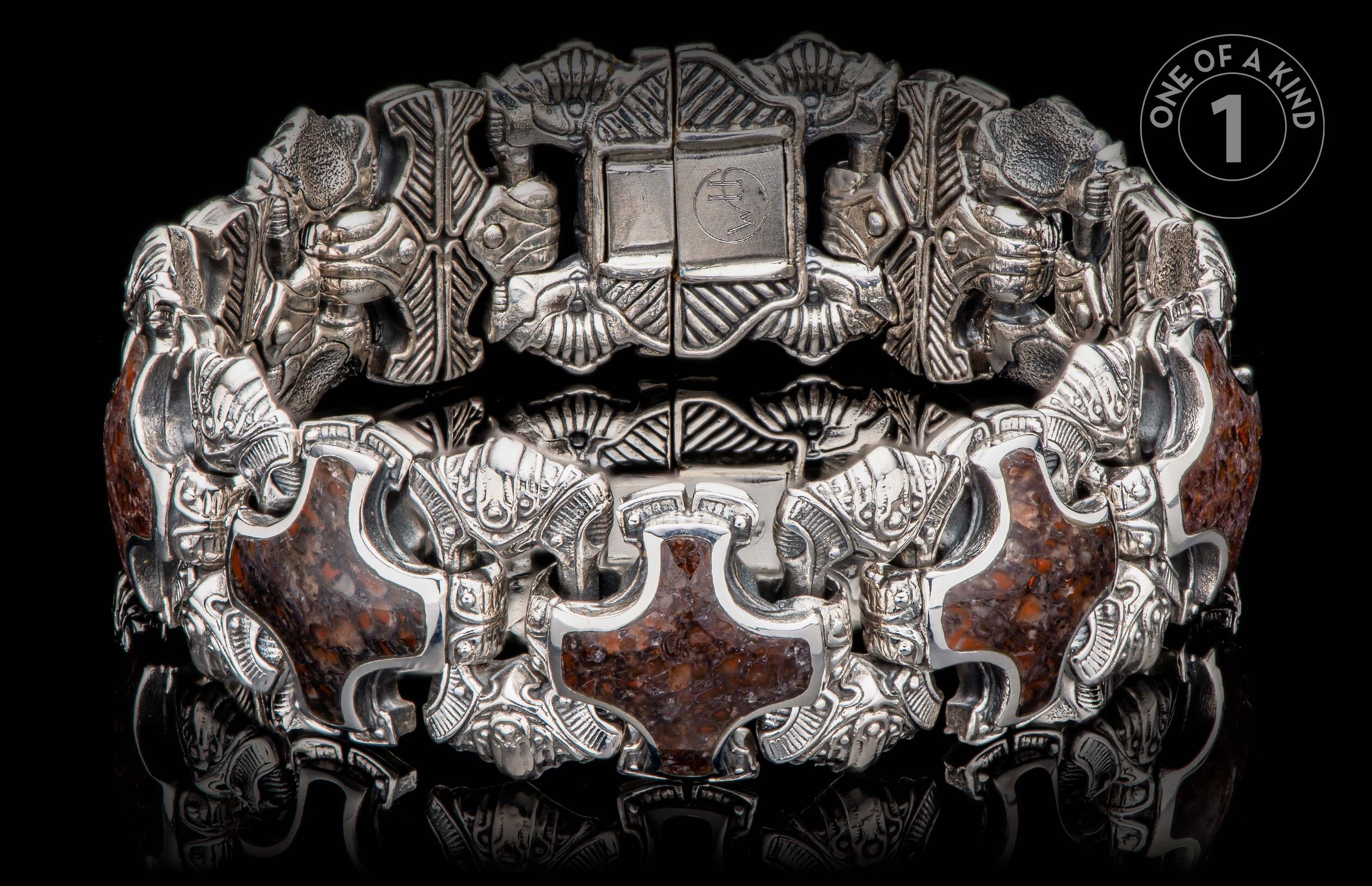 Ornate silver-toned bracelet with dark reddish-brown stone inlays, featuring intricate carved figures and a prominent clasp with "WH" initials.