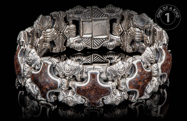 Ornate silver-toned bracelet with dark reddish-brown stone inlays, featuring intricate carved figures and a prominent clasp with "WH" initials.