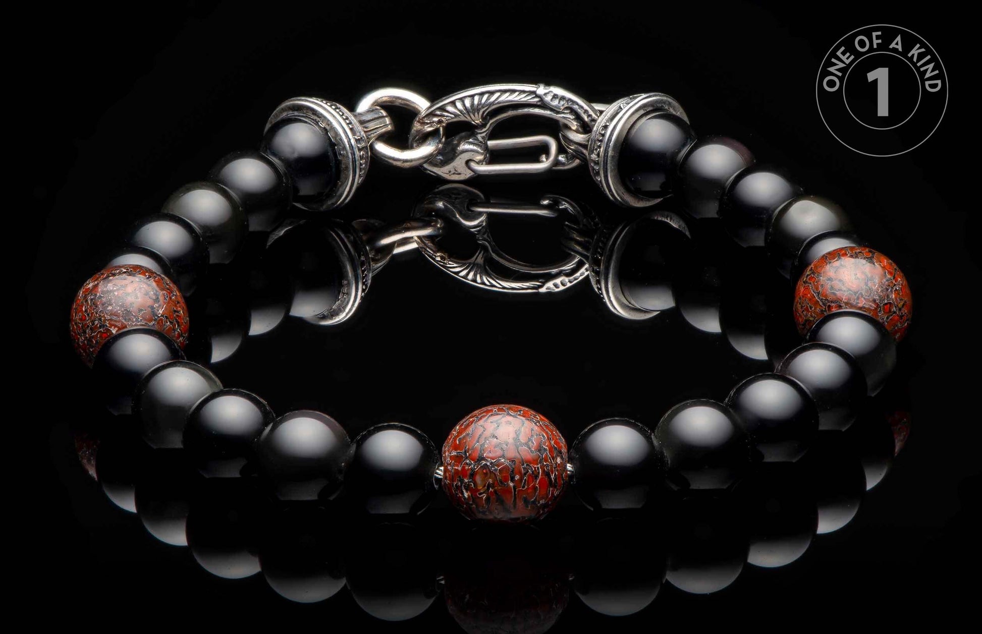 Black beaded bracelet with a central red patterned bead and an ornate silver clasp, reflected on a dark surface.