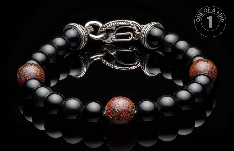 Black beaded bracelet with a central red patterned bead and an ornate silver clasp, reflected on a dark surface.