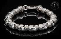 Silver-tone and marbled stone bracelet with skull beads and an ornate clasp, lying on a reflective black surface.