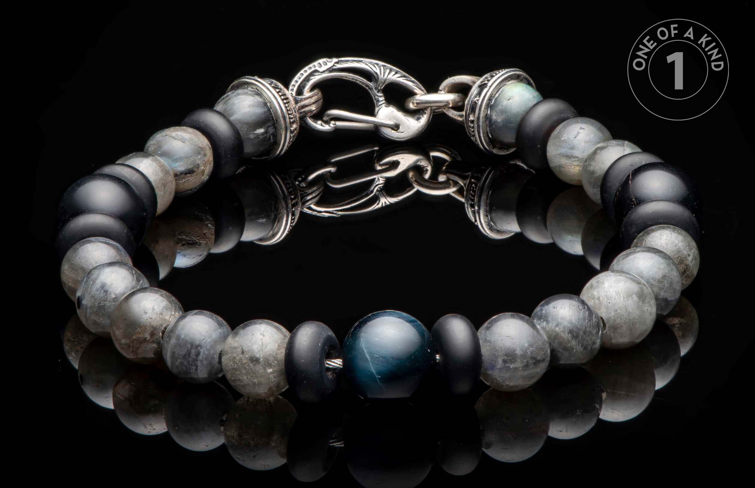 Beaded bracelet with black, grey, and blue stone beads and an ornate silver clasp, reflecting on a dark surface.