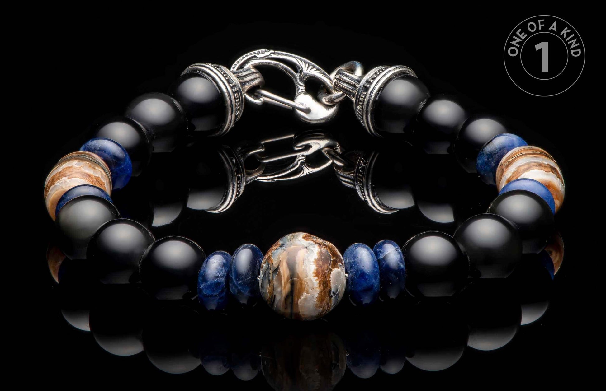Beaded bracelet with black onyx, blue sodalite, and central fossil mammoth tusk, silver-toned clasp, displayed on a reflective surface with a 'ONE OF A KIND' logo.