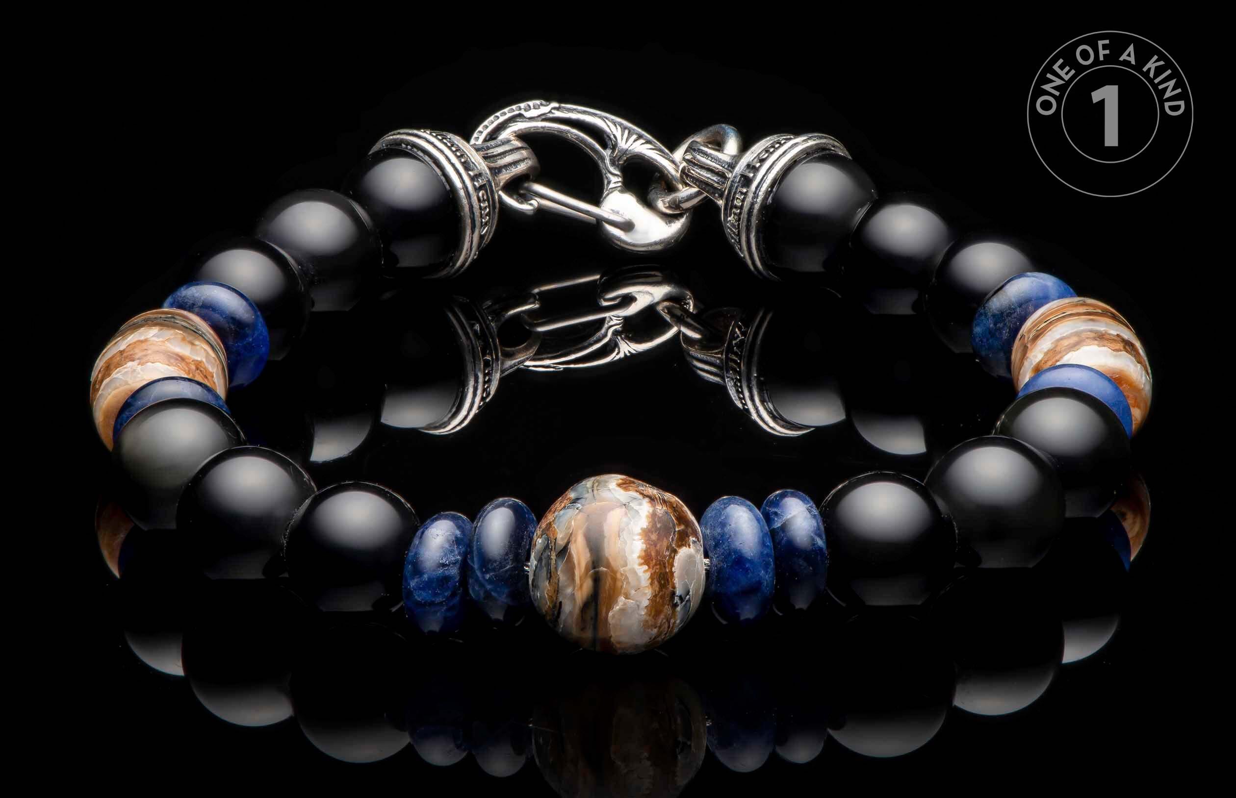 Beaded bracelet with black onyx, blue sodalite, and central fossil mammoth tusk, silver-toned clasp, displayed on a reflective surface with a 'ONE OF A KIND' logo.