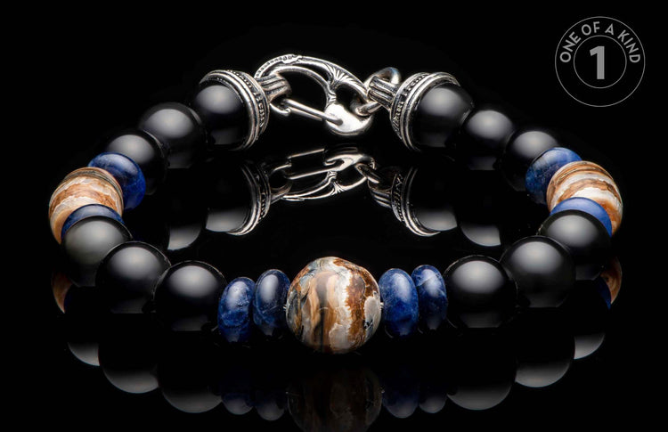 Beaded bracelet with black onyx, blue sodalite, and central fossil mammoth tusk, silver-toned clasp, displayed on a reflective surface with a 'ONE OF A KIND' logo.