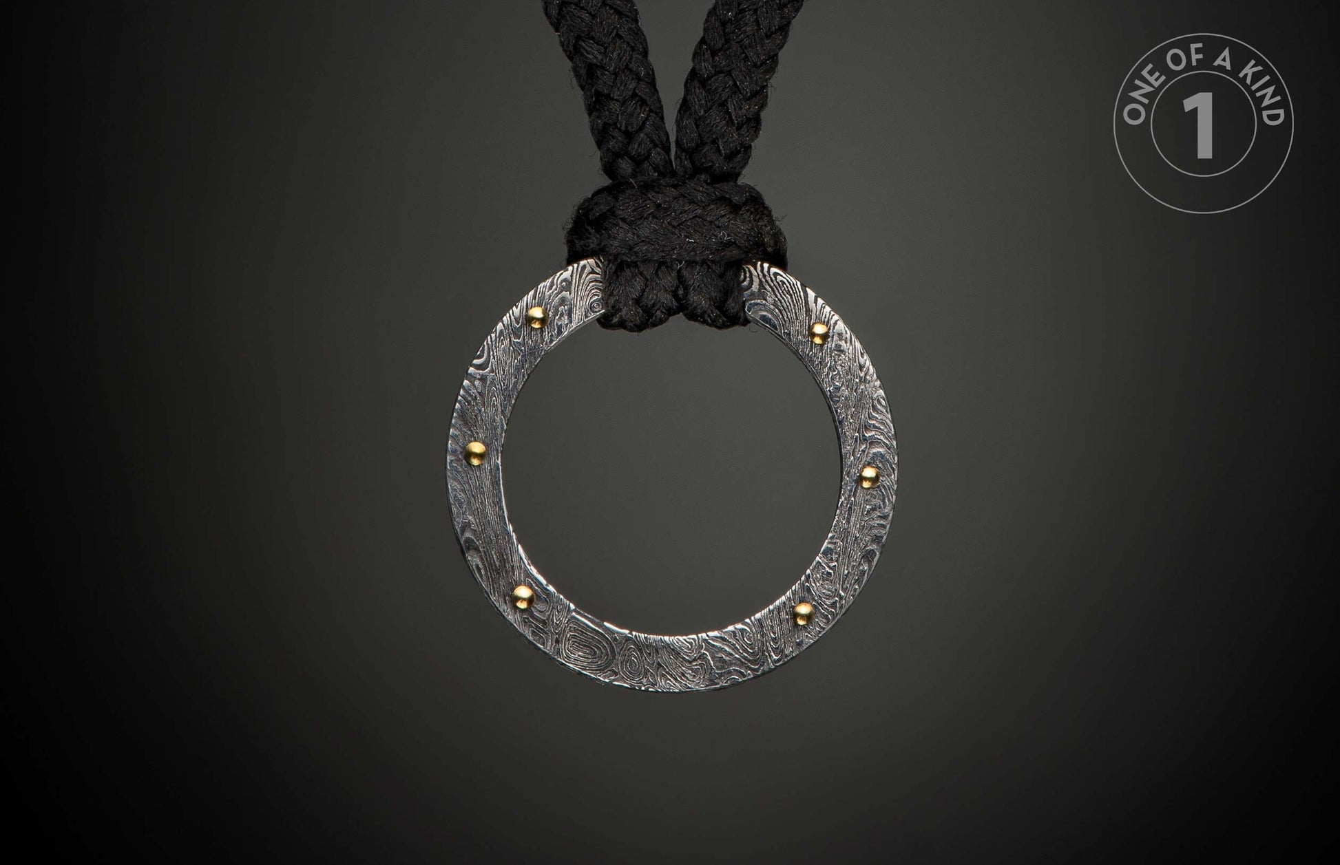 Damascus steel ring pendant with swirling patterns and gold rivets, suspended from a black braided rope.