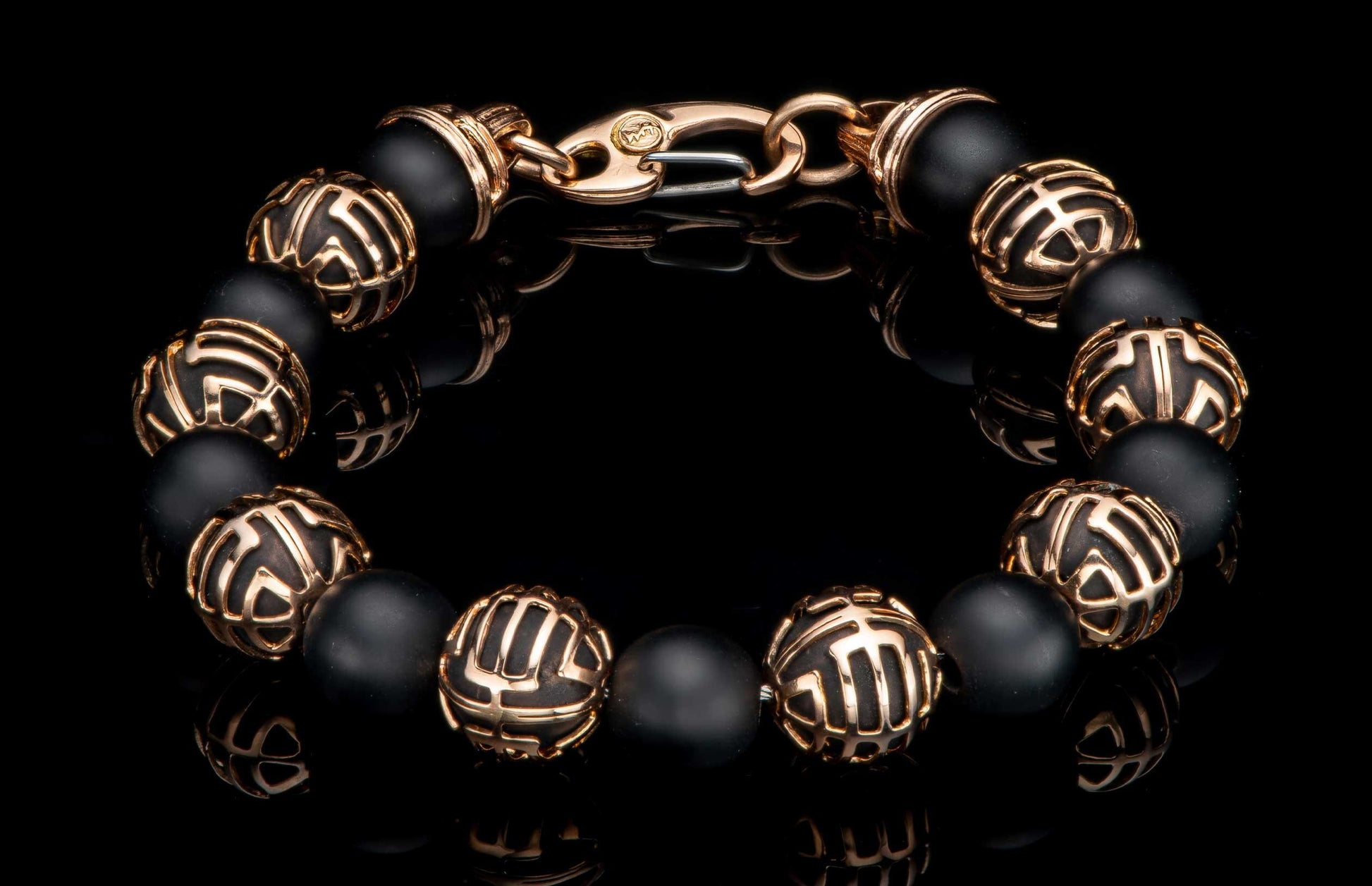 Black matte beaded bracelet with patterned rose gold metal beads and a rose gold lobster clasp on a reflective surface.